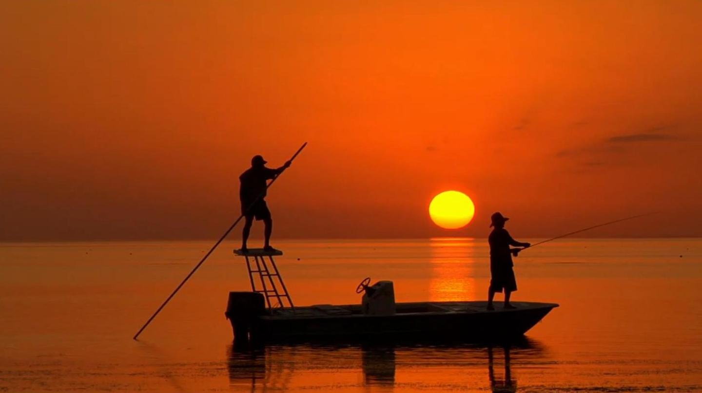 Sunset silhouette of two people fishing on a boat.