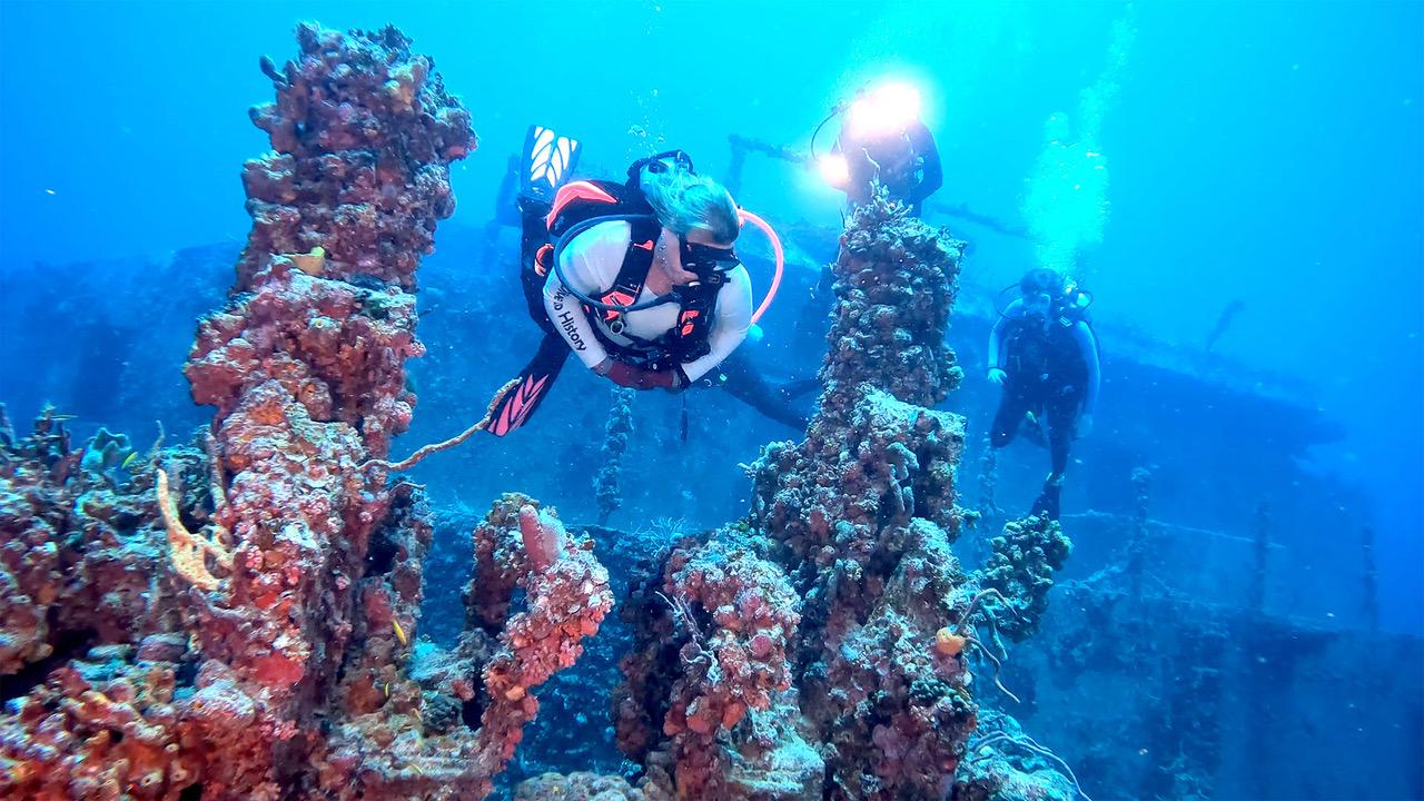 Divers exploring coral reef in clear blue water, with sunlight filtering through.