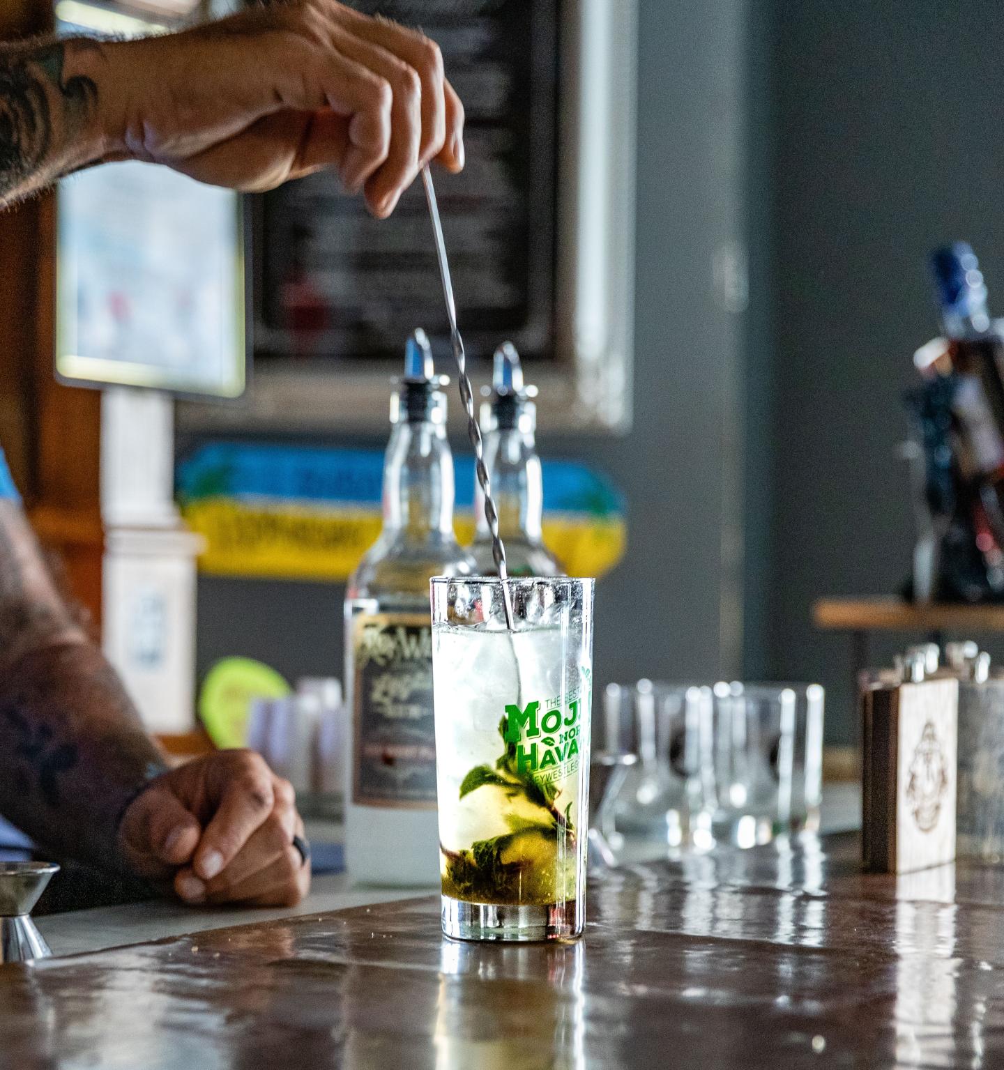 Making a mojito cocktail at a bar with bottles and glassware in the background.