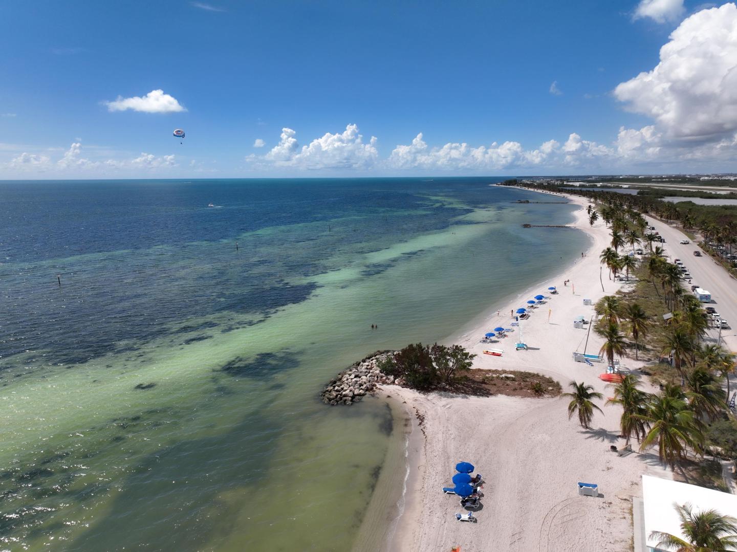 Aerial view of a beach with blue umbrellas and calm turquoise water.