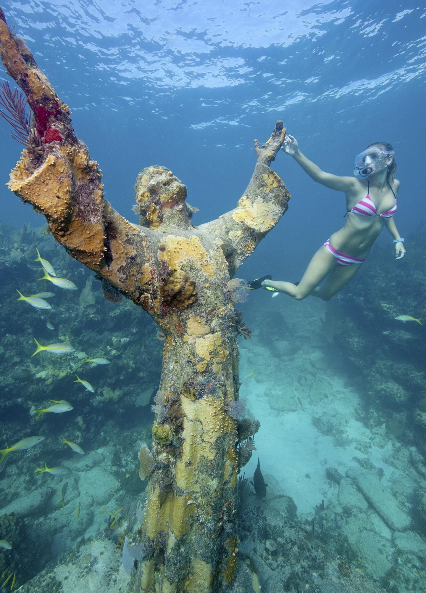 Underwater statue with arms raised, diver in snorkel gear nearby.
