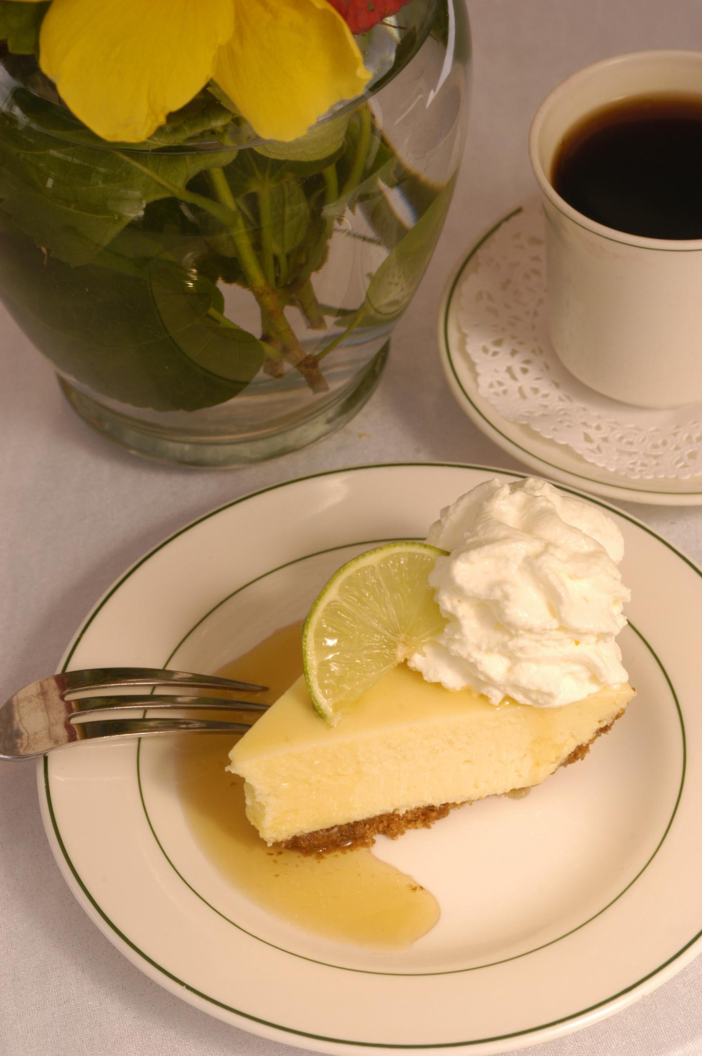 Key lime pie with whipped cream and lime on a plate, coffee cup nearby.