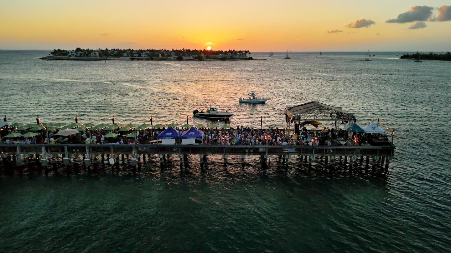Sunset over a pier with people, boats, and distant islands.