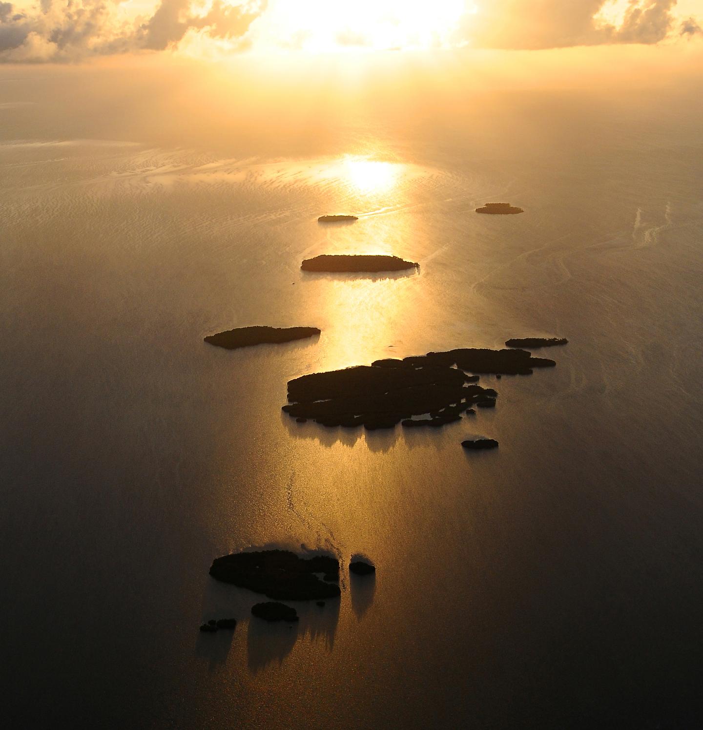 Sunset over a chain of small islands with golden reflections on the sea.