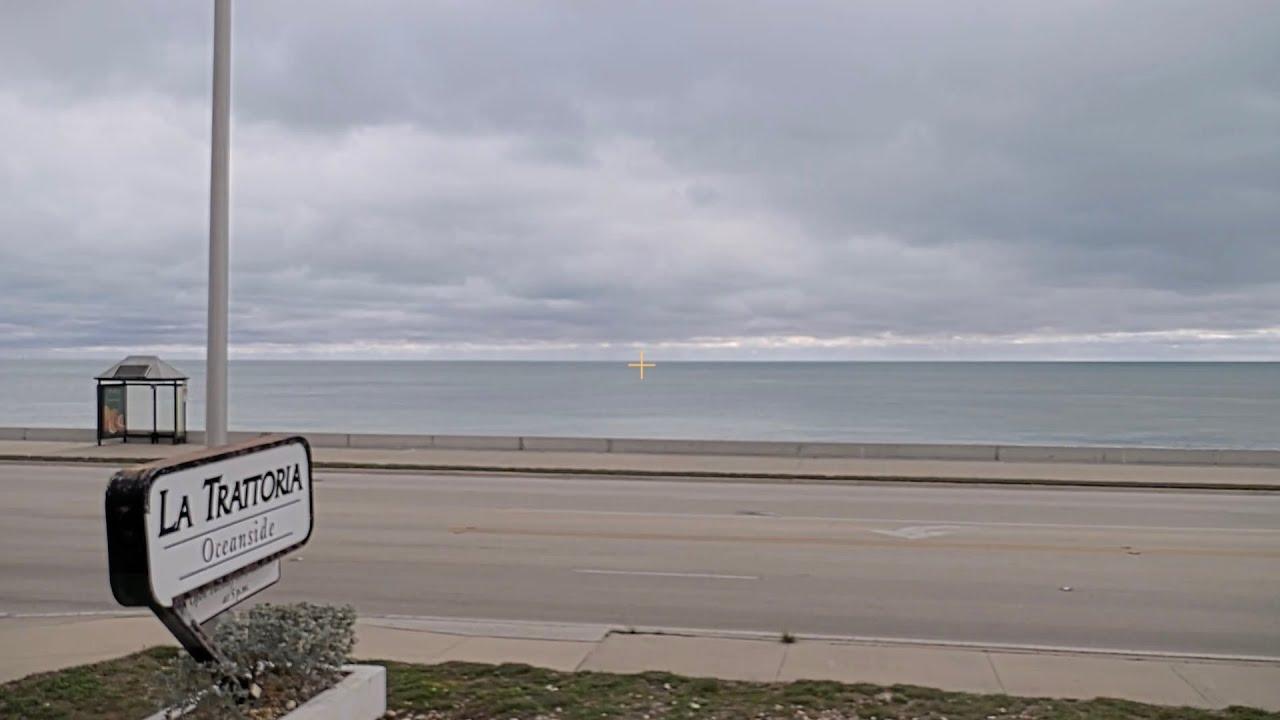 Coastal road with a restaurant sign, cloudy sky, and calm sea.