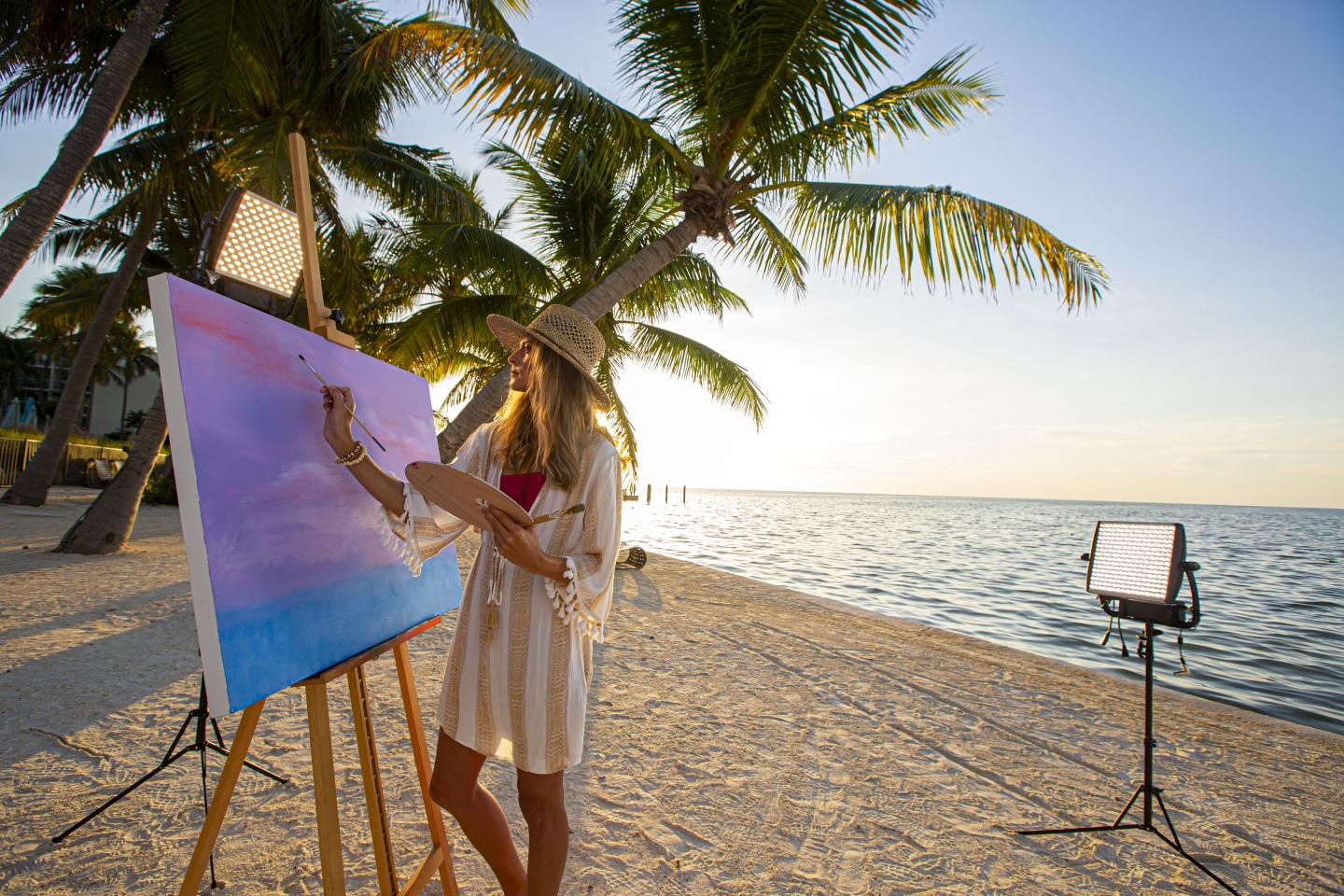 Artist painting a canvas on a tropical beach at sunset.
