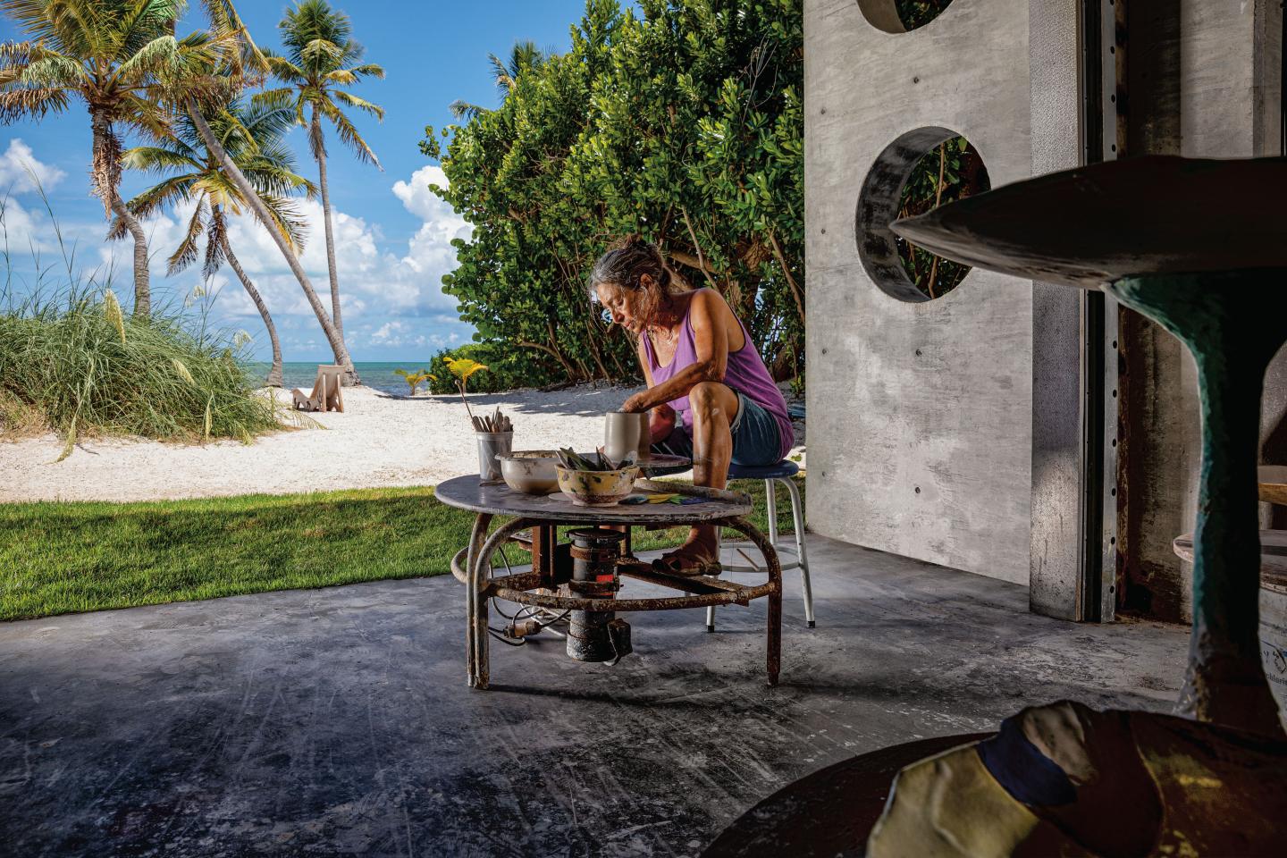Person sitting at a table crafting with trees and beach in the background.