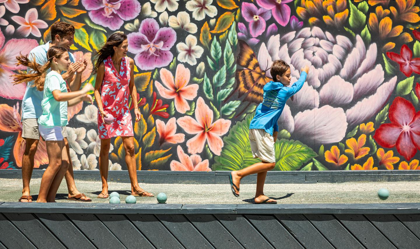 Children play bocce in front of a colorful floral mural.