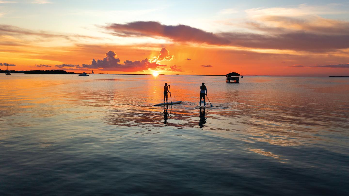 Two people paddleboarding on calm water at sunset.