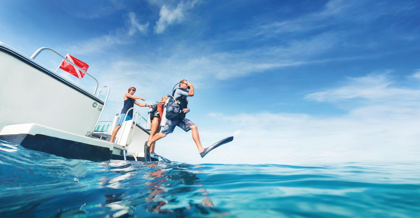 Person jumping from boat into clear blue ocean.