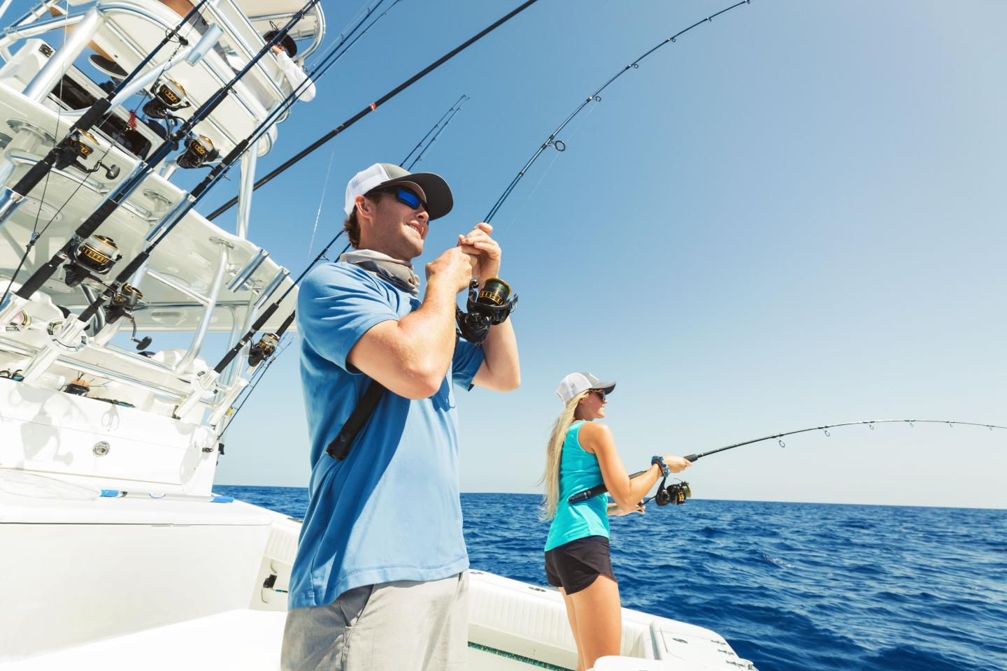 Two people fishing on a boat under a clear blue sky.