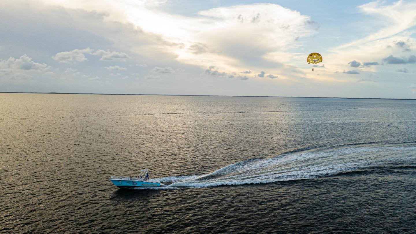 Boat and parasailer over calm ocean at sunset, clouds in the sky.