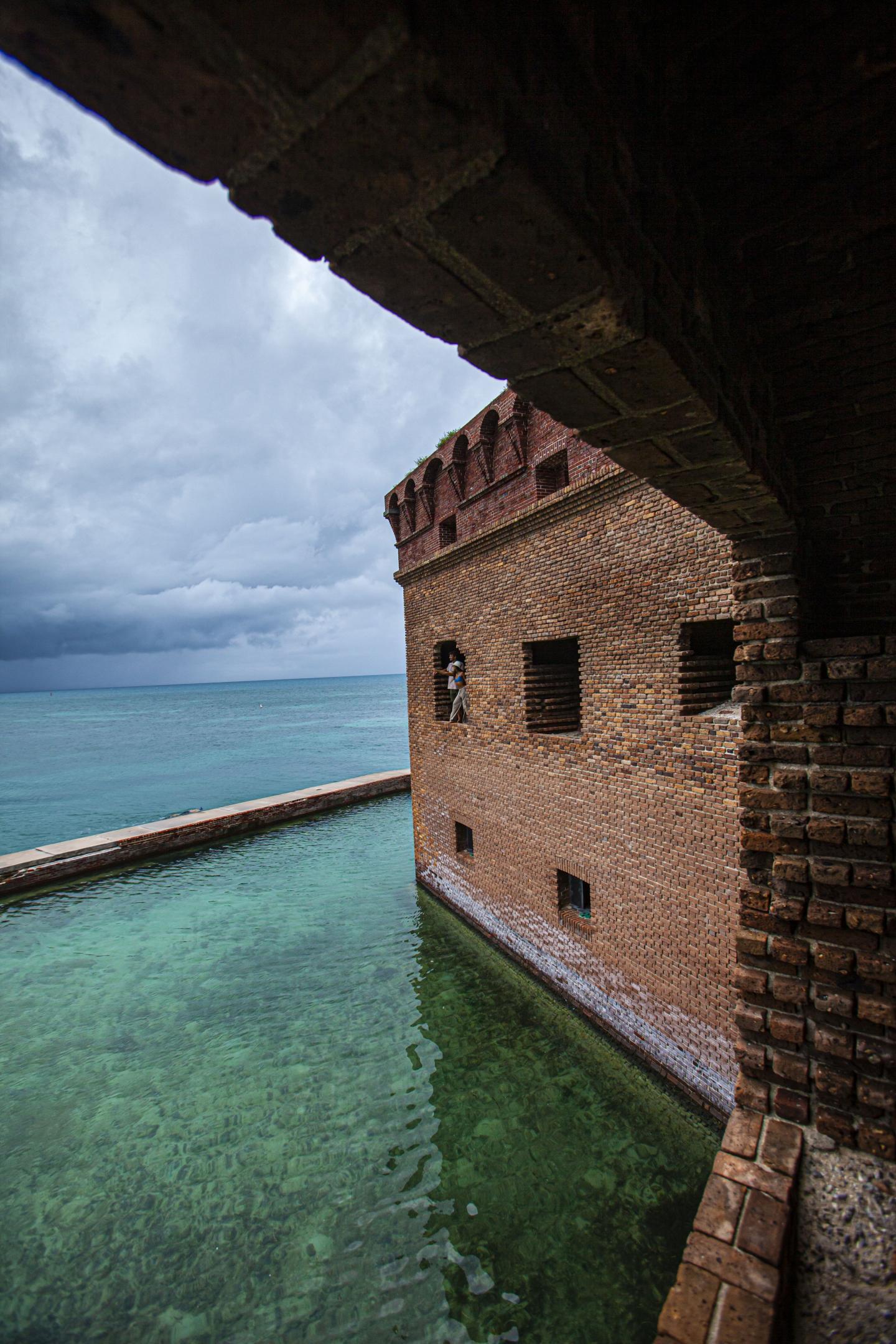 Brick fort corridor overlooking turquoise sea under cloudy sky.