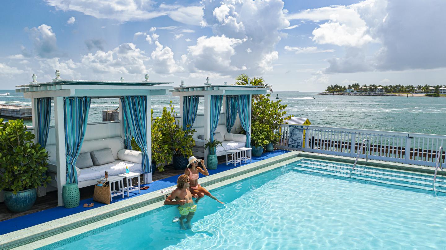 Man cleaning a pool near cabanas overlooking a scenic ocean view.