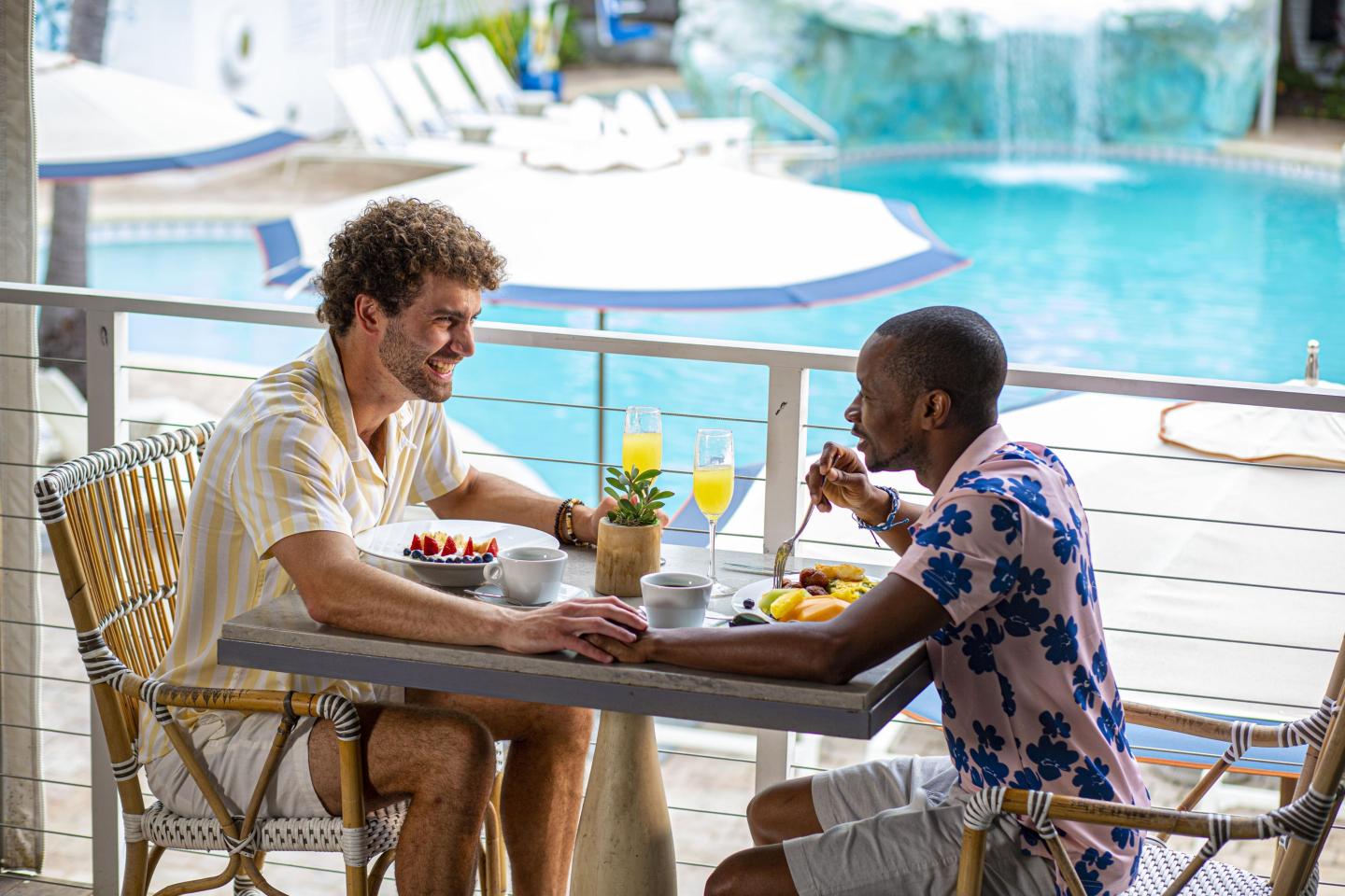 Two people enjoy breakfast at a poolside table.