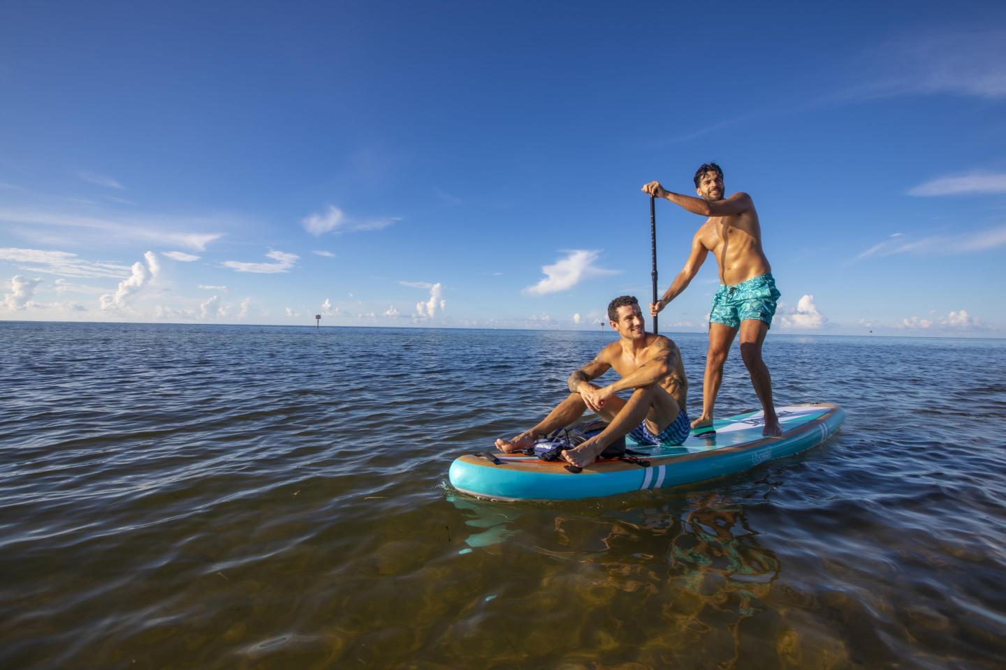 Two men paddleboarding on a calm sea under a clear blue sky.