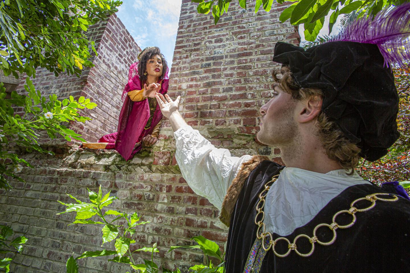 Man in Renaissance costume reaching for a woman above a brick wall.