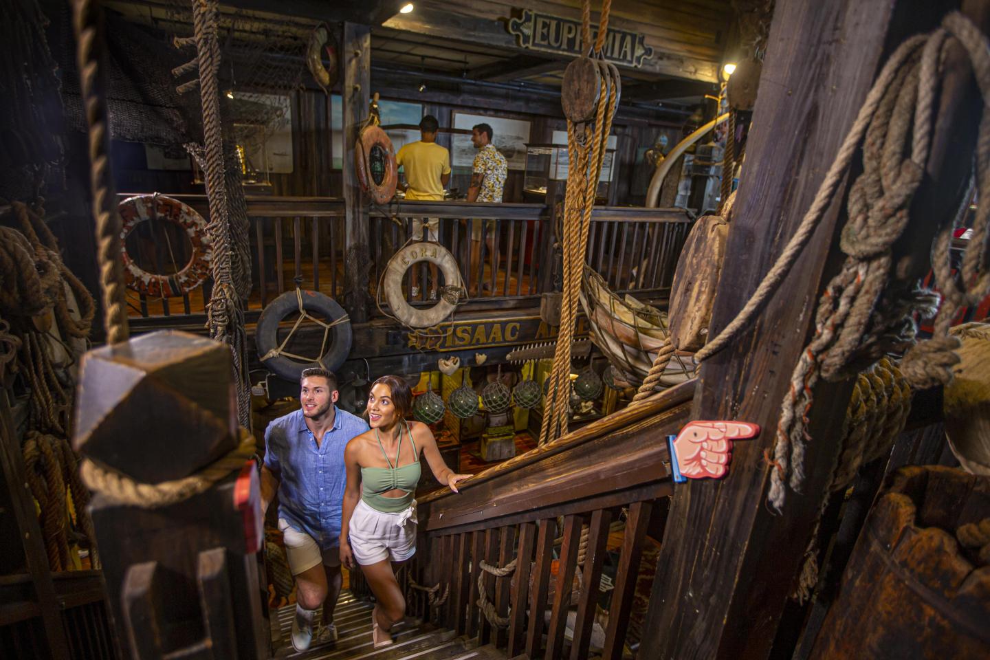 Couple descending wooden ship-themed stairway with nautical decor.