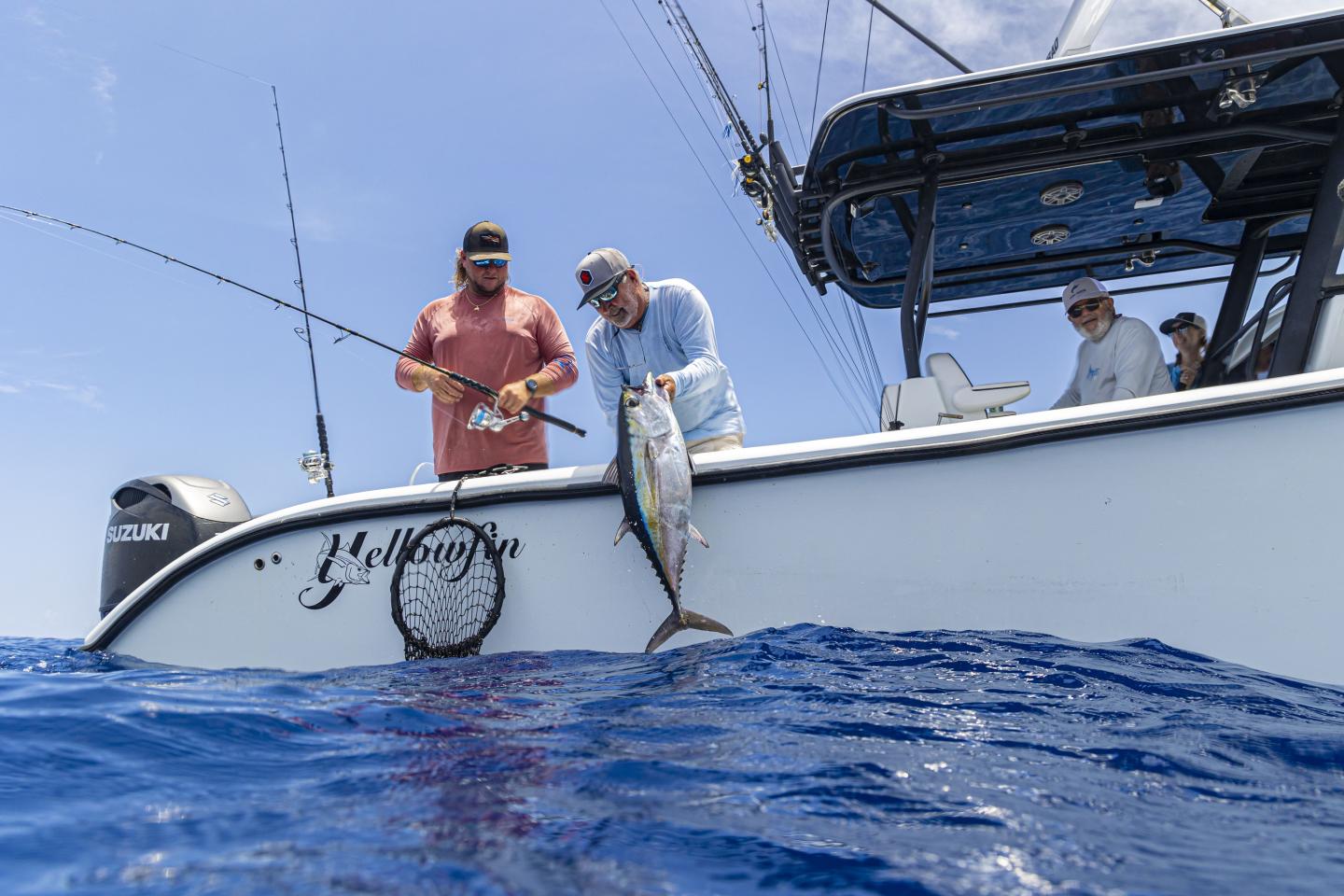 Two men fishing on a boat, one holding a large fish over the water.