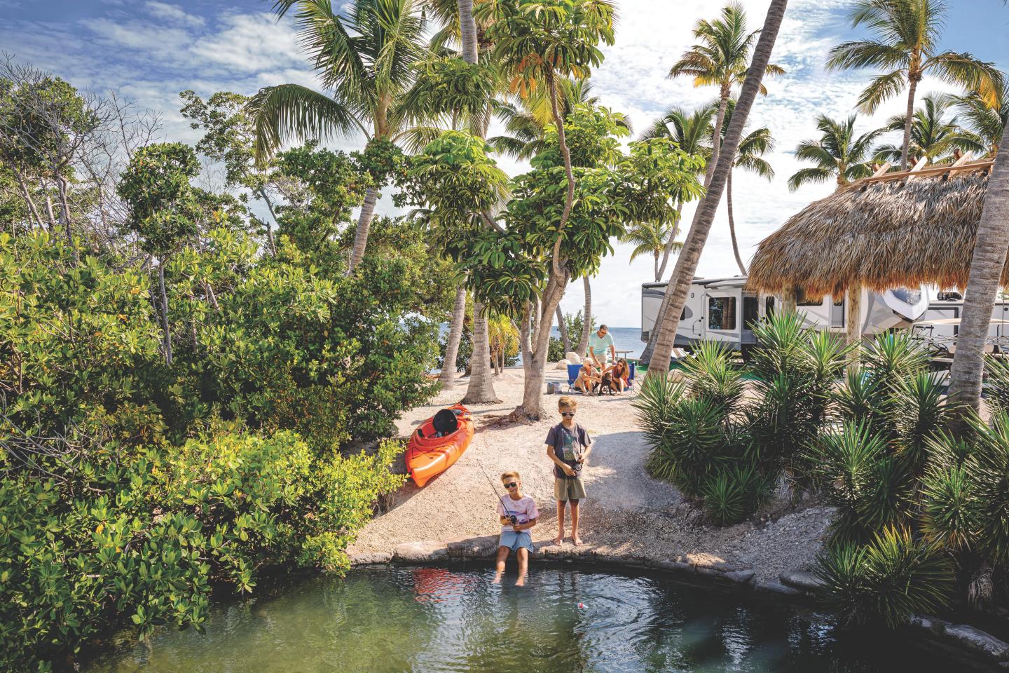 Tropical scene with two people near a lagoon, palm trees, and a red kayak.