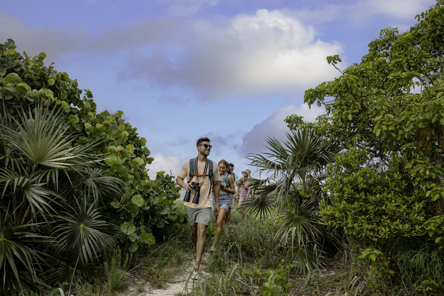 People hiking through lush greenery under a partly cloudy sky.