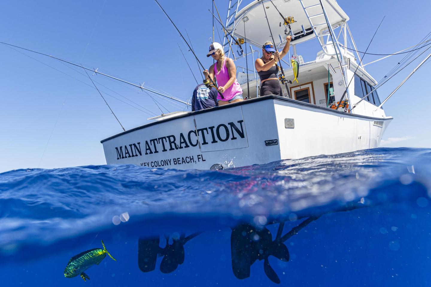 Fishing boat with two people, underwater view of a fish, clear blue water.