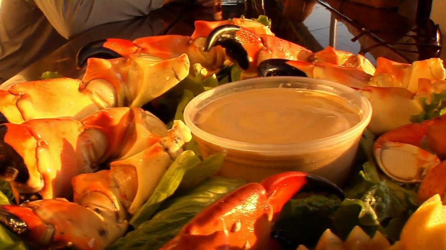 Stone crab claws and dipping sauce on a platter, sunlit setting.