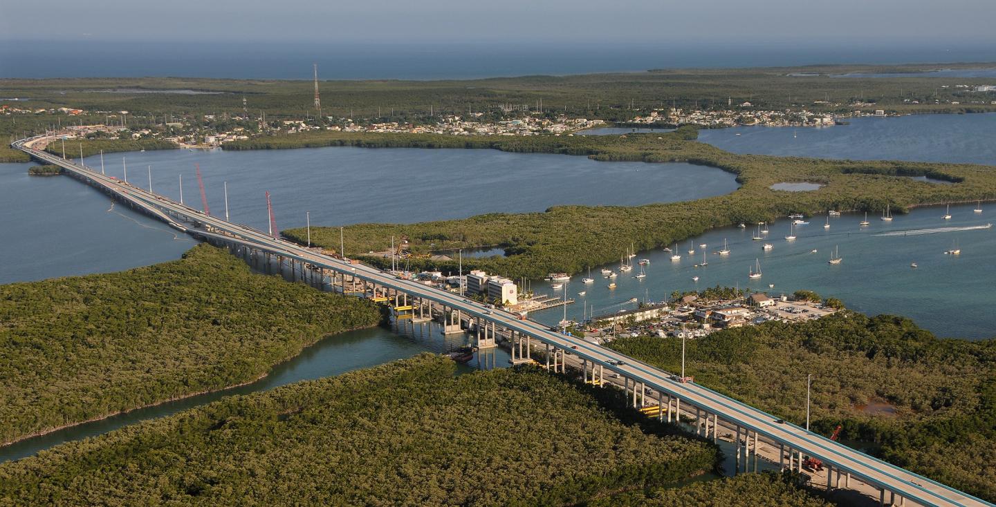 Aerial view of a long bridge over lush green islands and waterways.