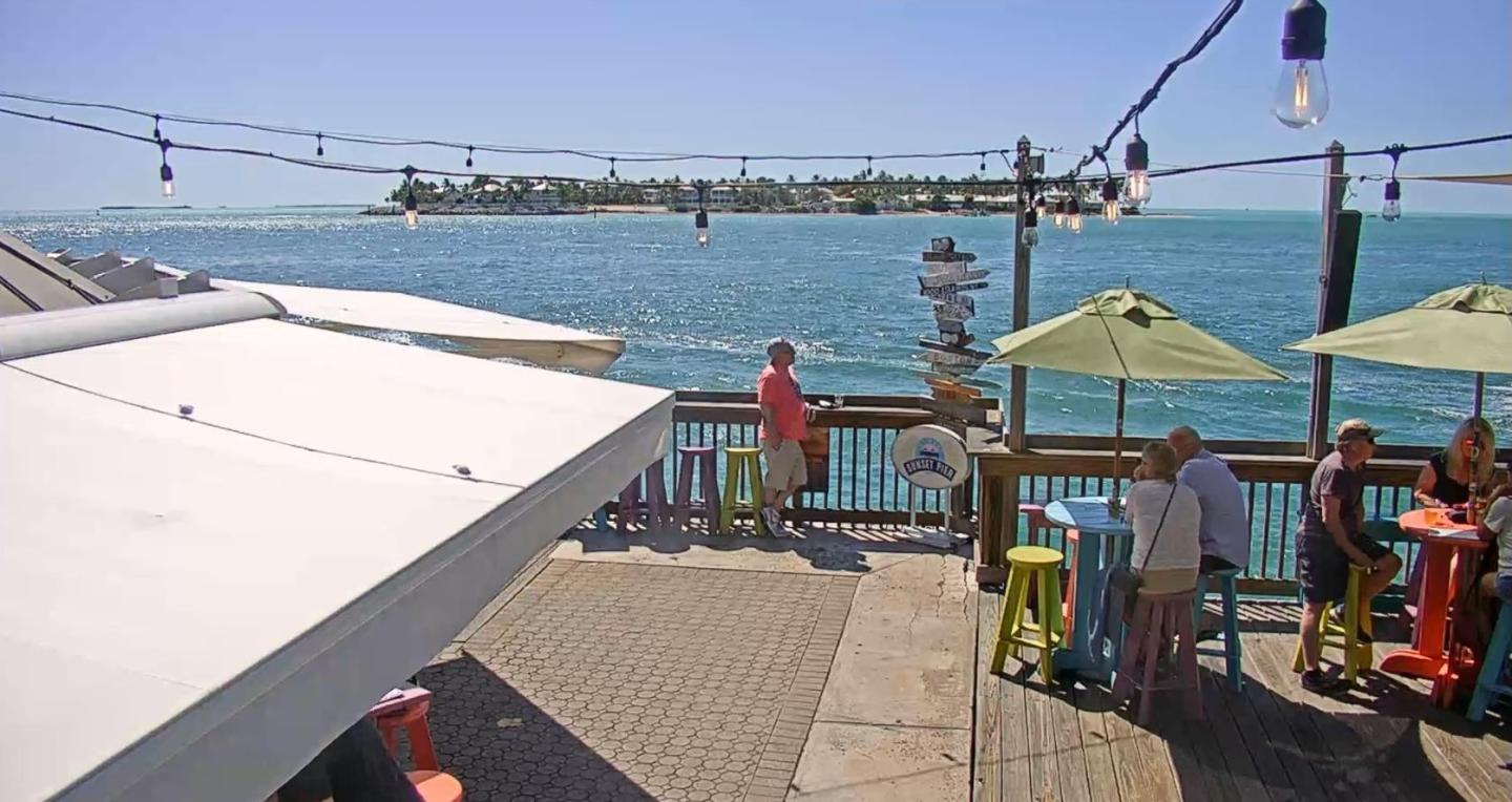 Outdoor seaside café with tables and umbrellas, ocean view in the background.