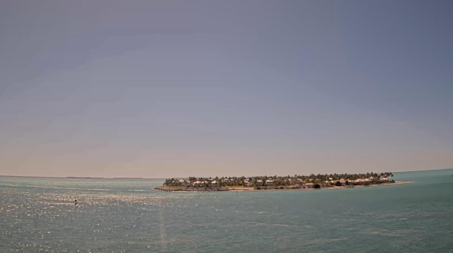 Calm turquoise sea with distant small island under clear blue sky.