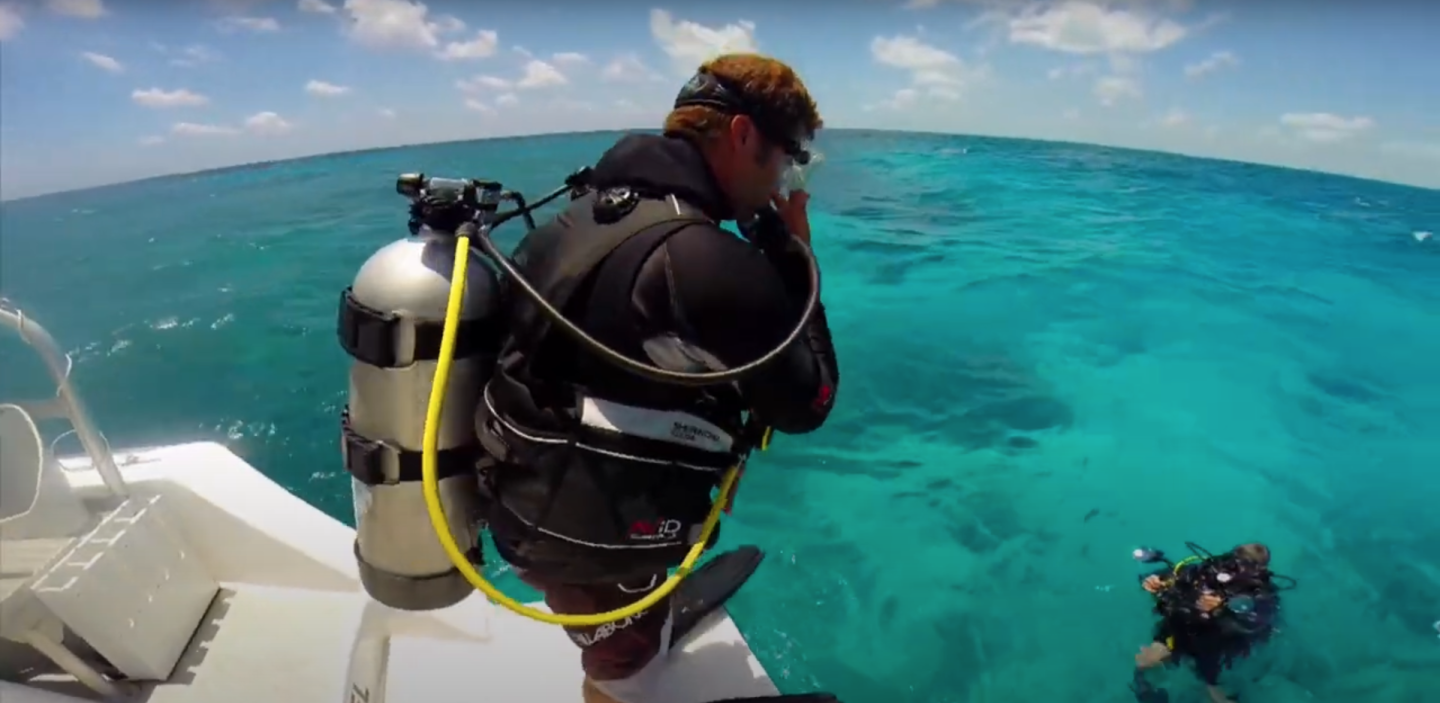 Scuba diver about to enter clear blue ocean from a boat.