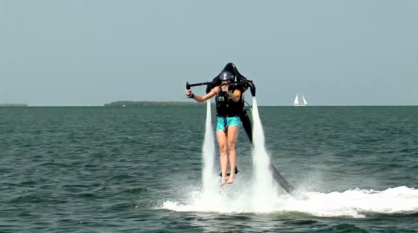 Person using a water jetpack above the ocean.