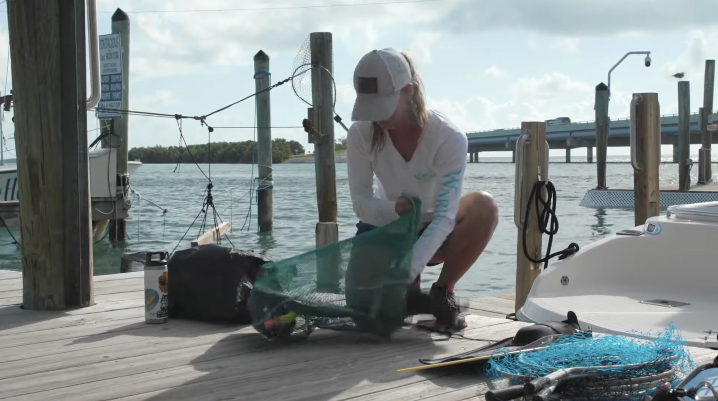 Woman on dock preparing fishing gear beside a boat.