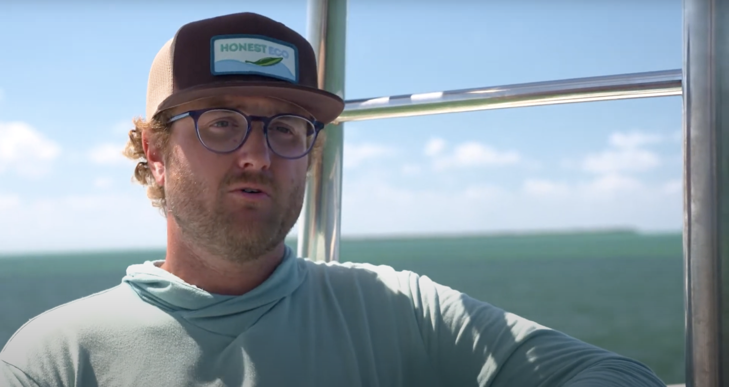 Man in sunglasses and cap on a boat with ocean view.