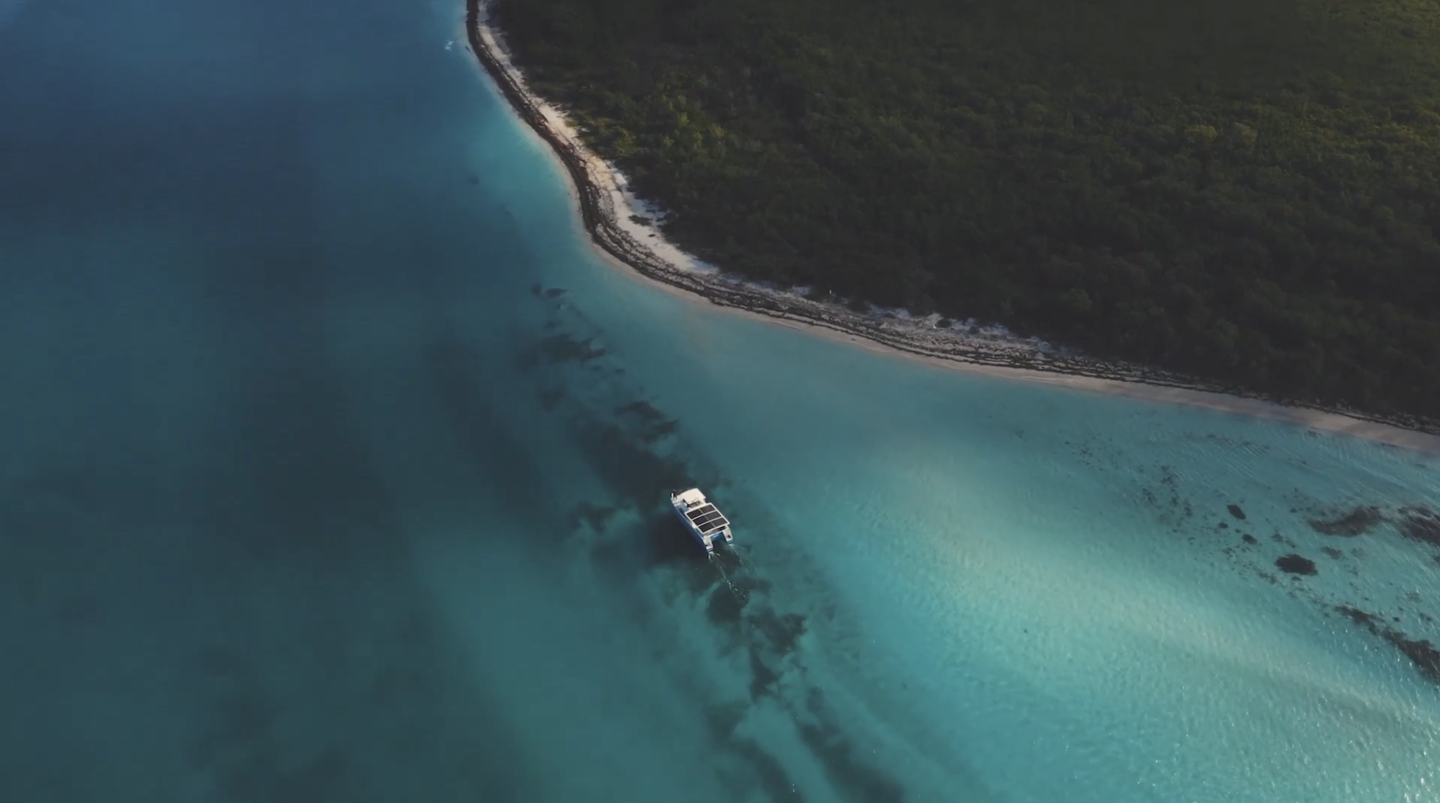 Aerial view of a yacht sailing in clear turquoise water near a lush green shoreline.