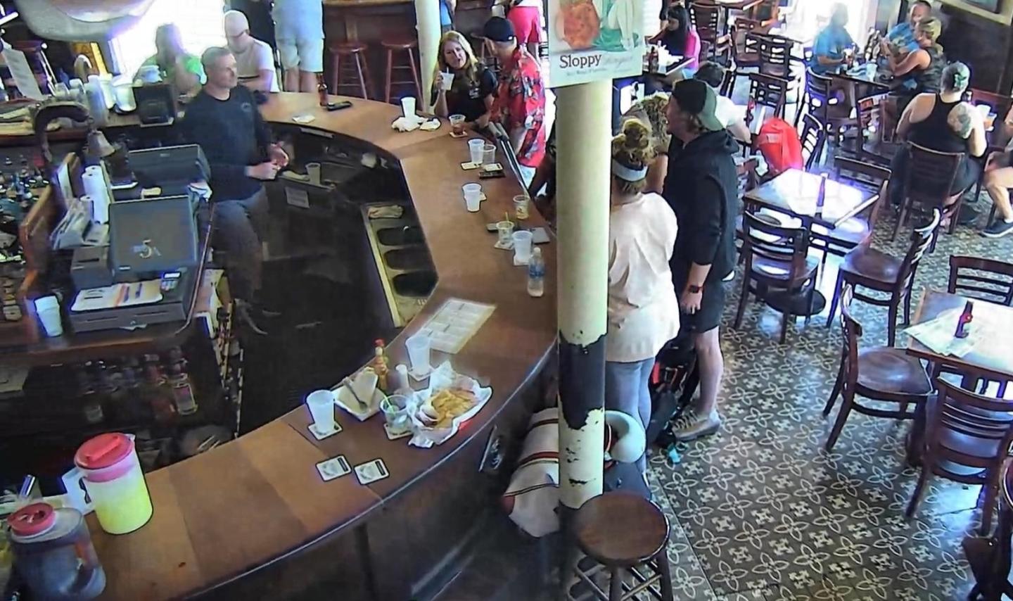 Busy café with patrons at a curved bar and tables, tiled floor.