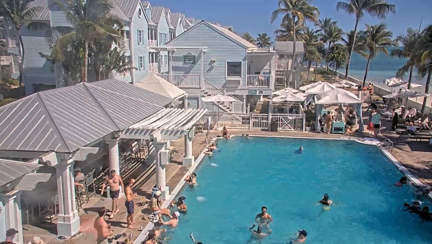 Outdoor pool at a seaside resort with people swimming and sunbathing.