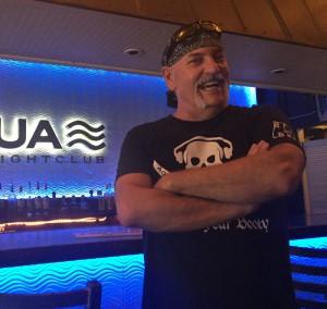 Man smiling with arms crossed in a nightclub with blue lighting.