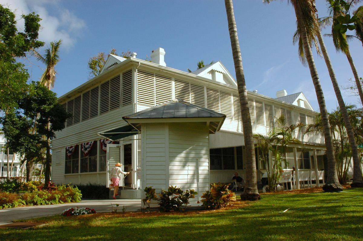 Large white house with palm trees and a manicured lawn, under a clear blue sky.