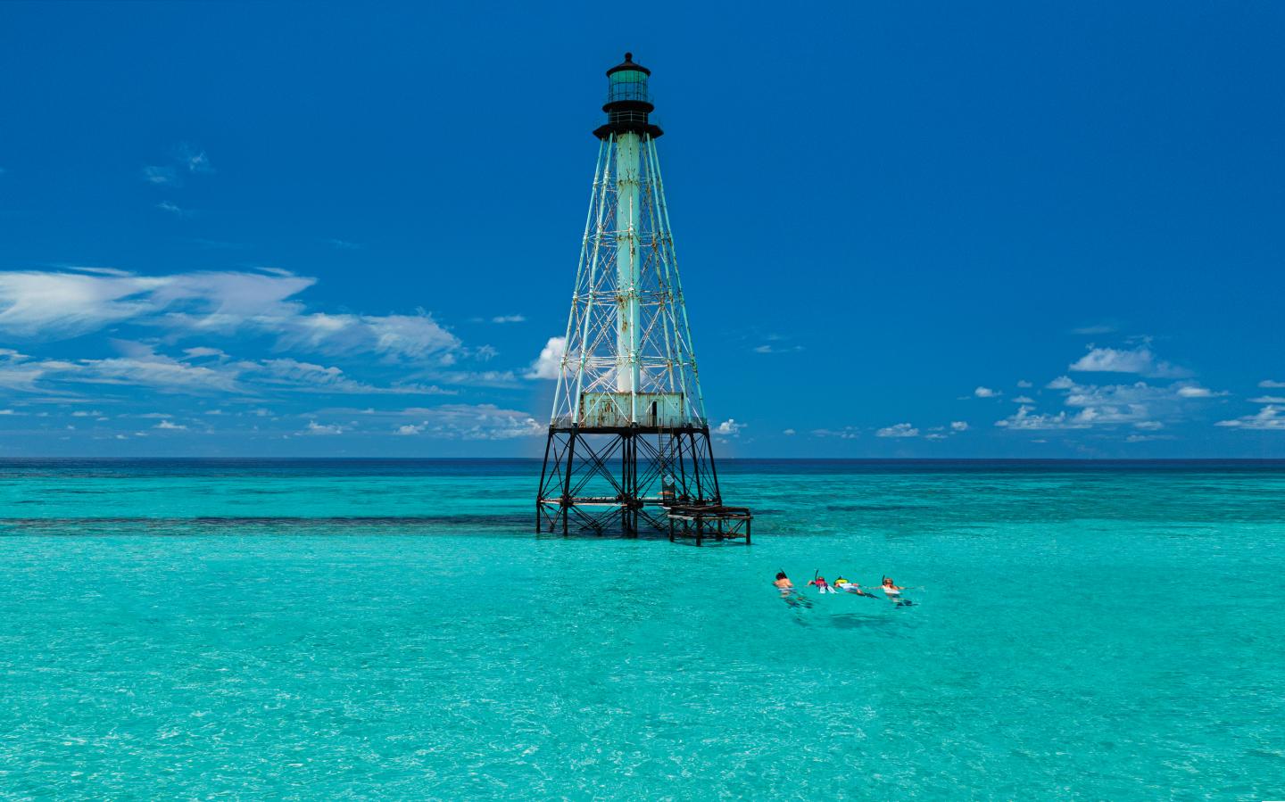 Turquoise ocean with swimmers near a tall, metal lighthouse.