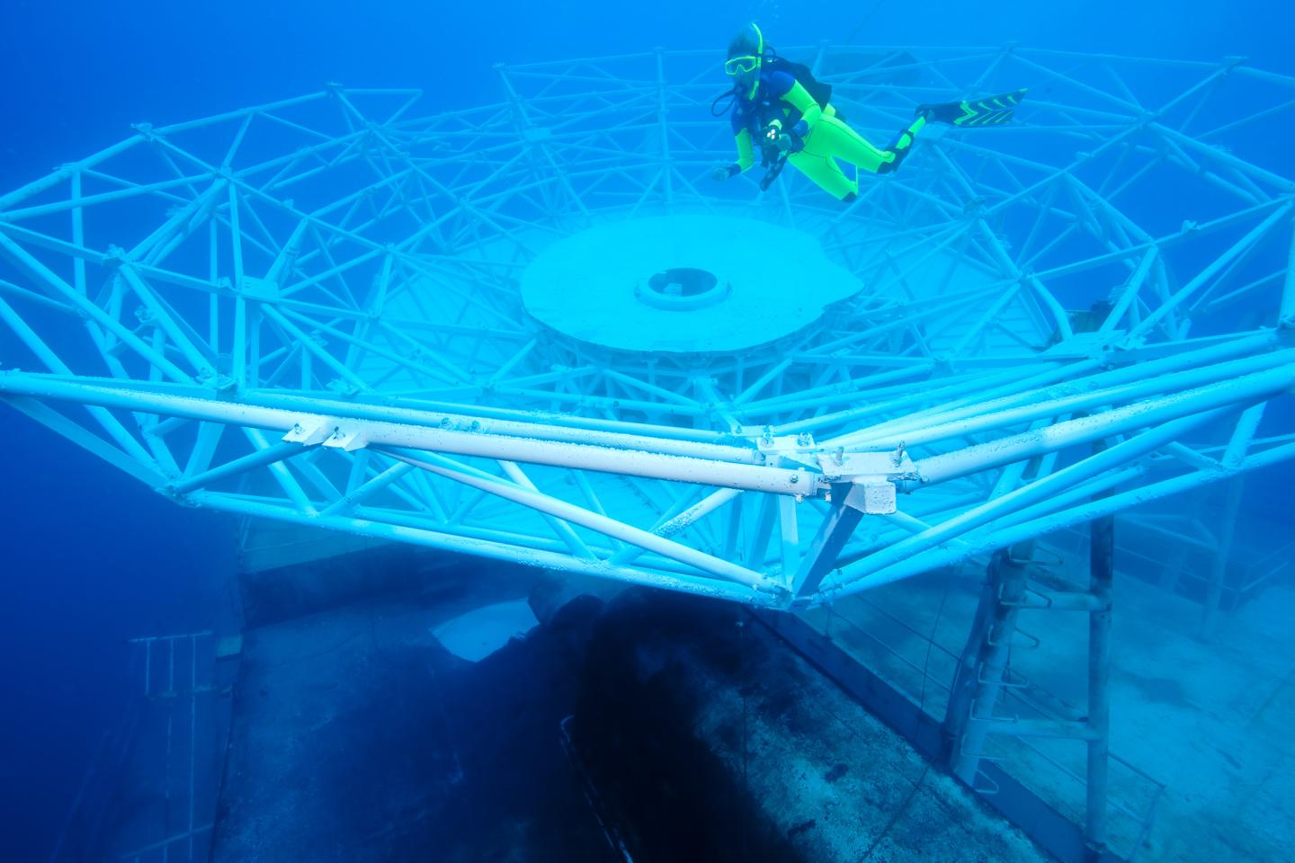 Diver exploring underwater metal structure in clear blue water.