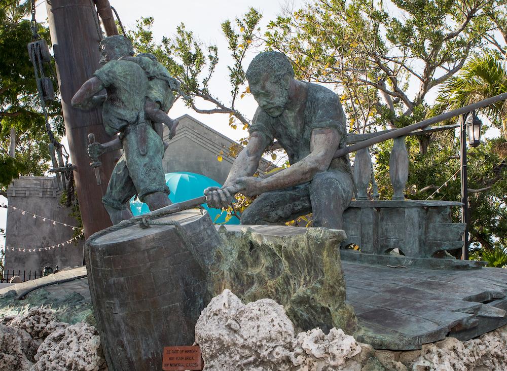 Two bronze statues of divers amid coral, one standing, one kneeling.