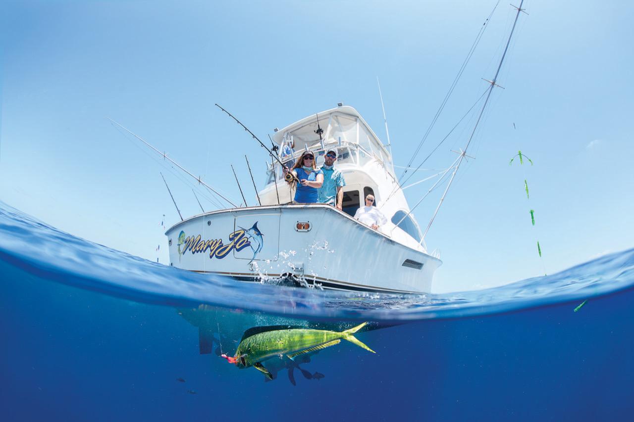 Fishing boat on ocean, fish swimming below, clear blue sky.