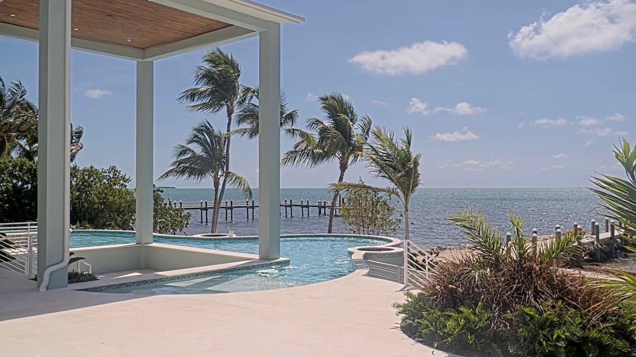 Tropical poolside with palm trees and ocean view under a clear blue sky.