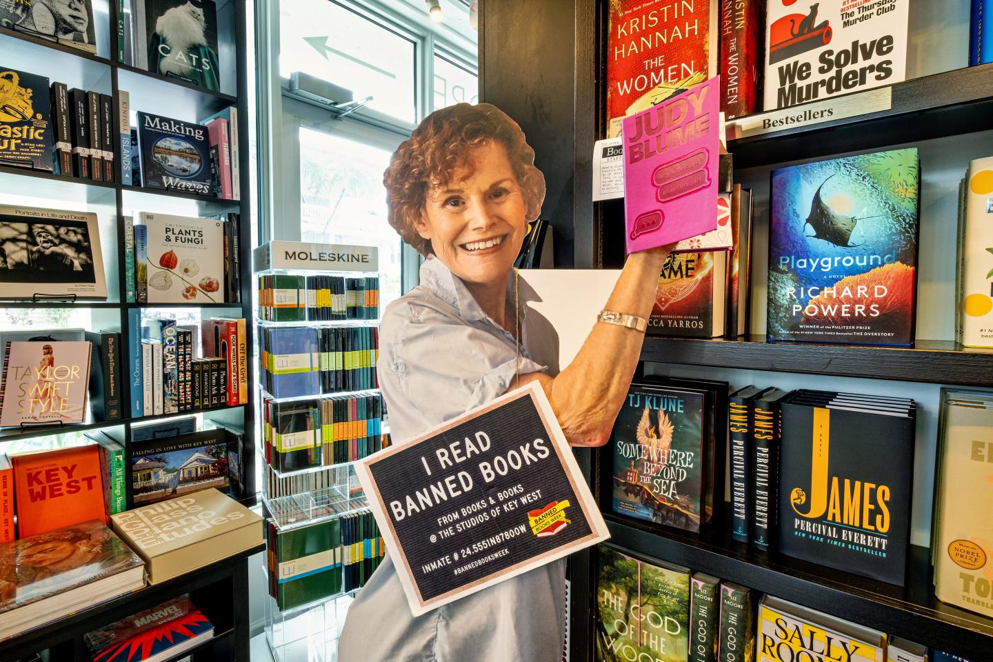 Cardboard cutout holding a pink book in a colorful bookstore.