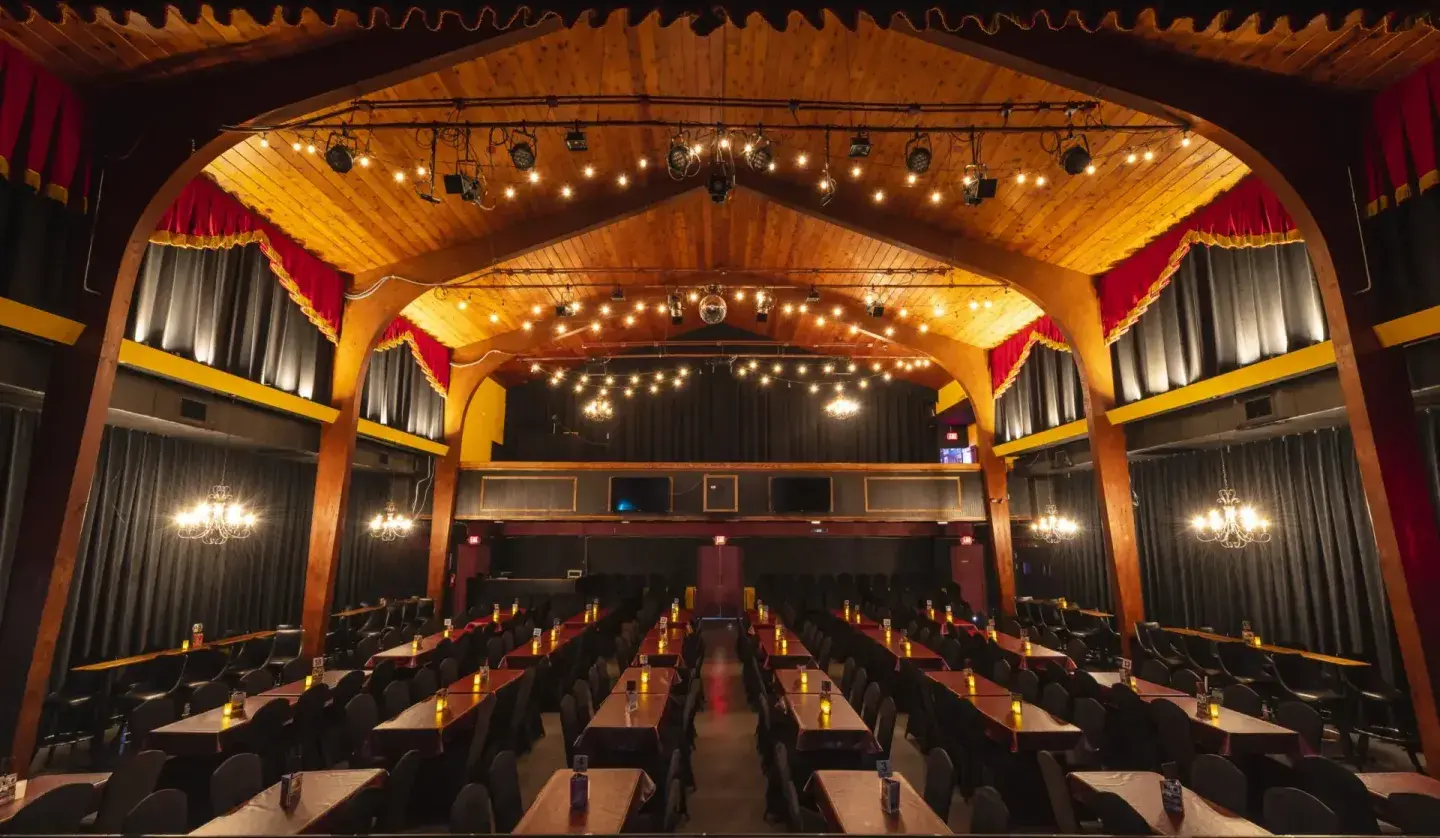 Elegant theater interior with rows of tables, red curtains, and warm lighting.