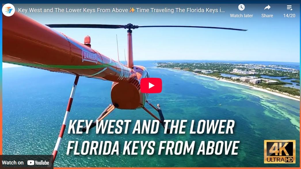 Red helicopter flying over blue ocean, sunny skies.