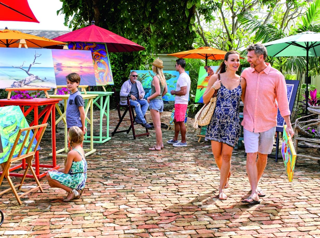 Outdoor art market with colorful umbrellas and people browsing paintings.