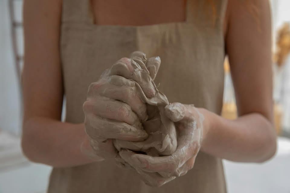 Hands molding clay, wearing a beige apron.