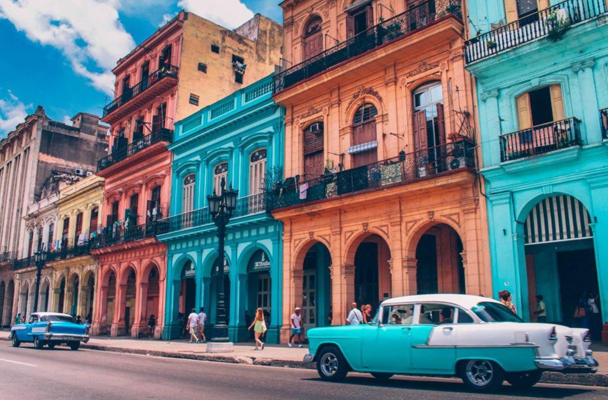 Colorful buildings line a street with vintage cars in front.